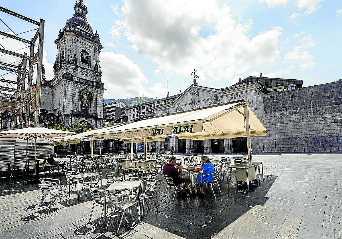 Una pareja se refugia del sol en una terraza con toldo en una desierta plaza de Elgoibar.