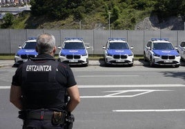 Un agente de la Ertzaintza ante varios vehículos policiales.
