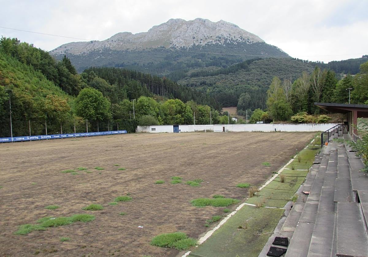 Césped completamente agostado del abandonado Atxabalpe con la peña de Udalatx al fondo.