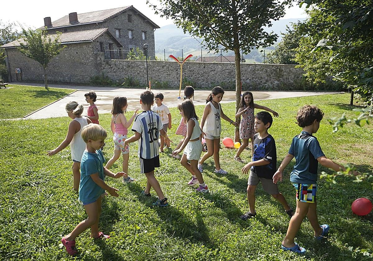 Imagen principal - Los niños y niñas disponen de un entorno natural privilegiado para jugar, junto a dos monitores, cuando sus padres están en clase y Oihane y Nekane atienden en clase, con los apuntes sobre la mesa. 