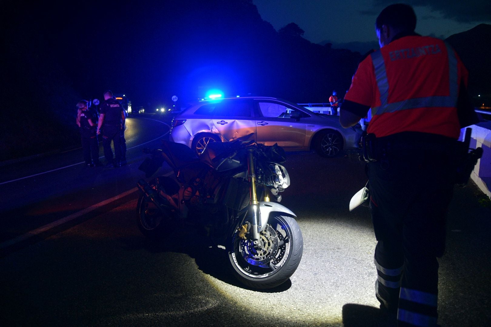 Un agente de la Ertzaintza fotografía la moto y el coche, claramente dañado en la parte derecha, afectados en el accidente en Deba.