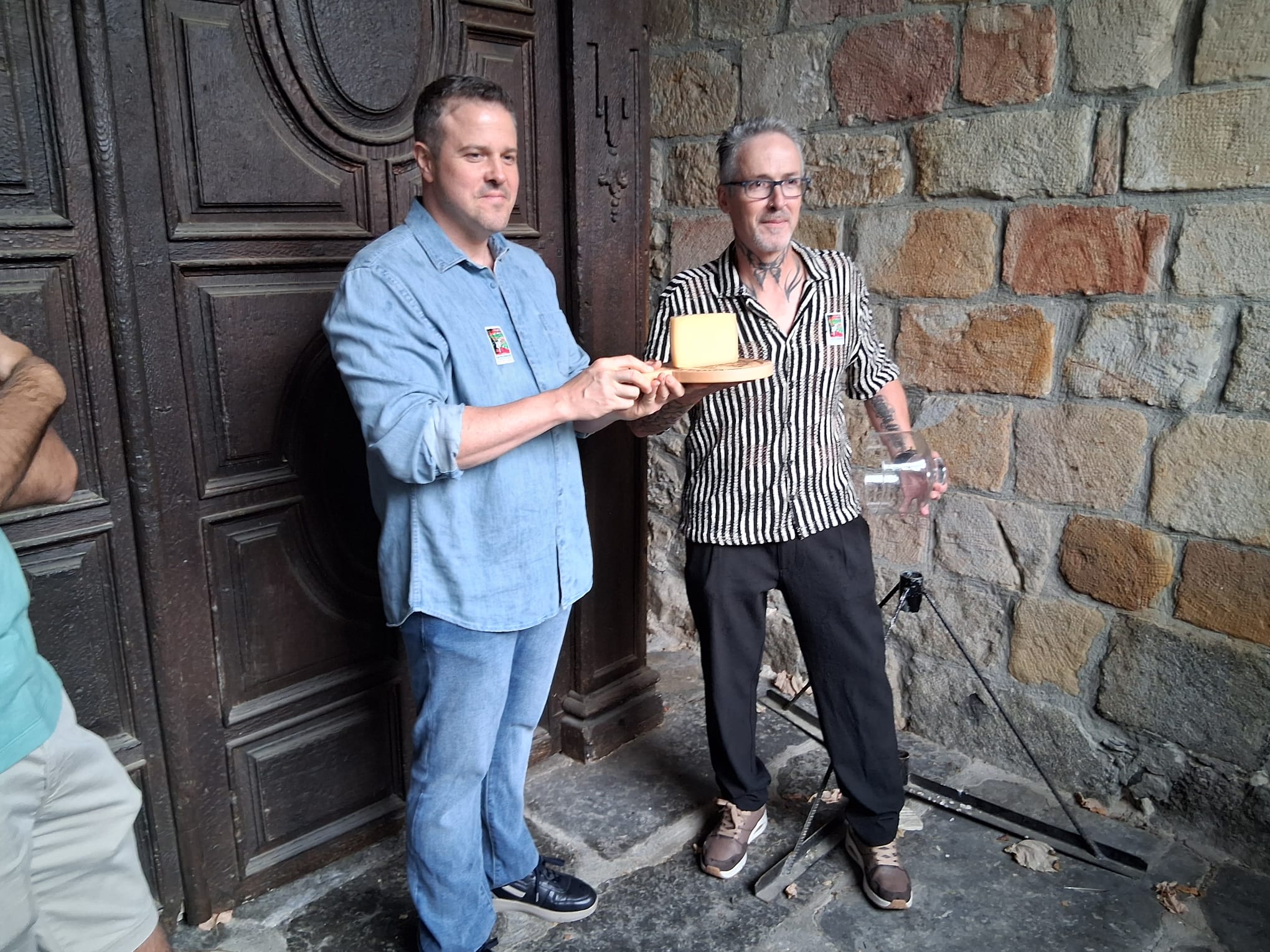 Imagen principal - Lekarozko Kortari gaztandegikoek egindako gazta irabazlearen erdia eskuan dutela erosleek.