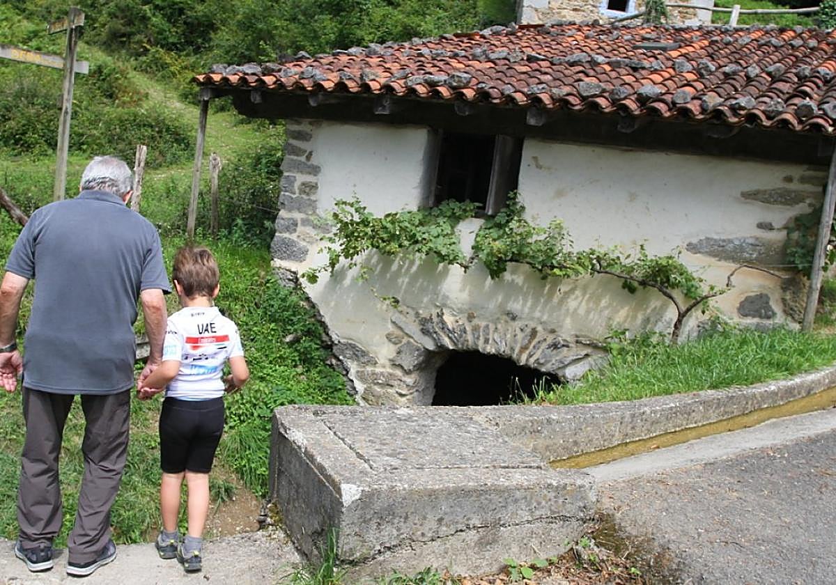 Un hombre contempla con su nieto el canal de agua, junto al histórico molino de Lastur.