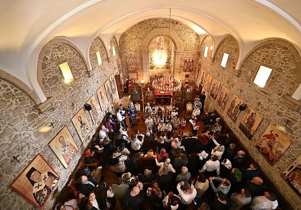 Fieles ortodoxos en la ermita de Uba de Martutene, mientras un coro de niños canta el himno de Rumanía frente al altar.
