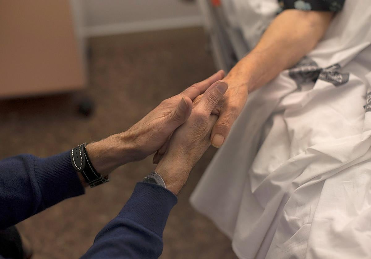 Un familiar sostiene la mano de una paciente en un hospital.