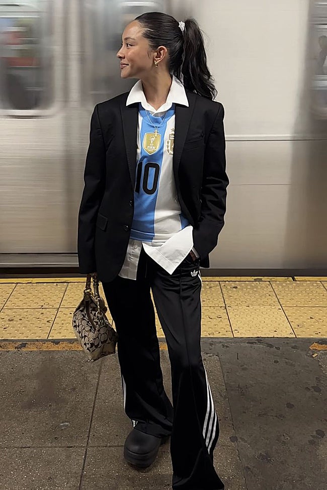 Una aficionada con una americana negra, camiseta de fútbol y pantalones negros de Adidas.