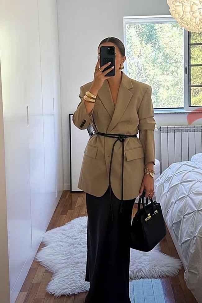 'Blazer' beige estructurado, cinturón de cuero fino y falda satinada negra.