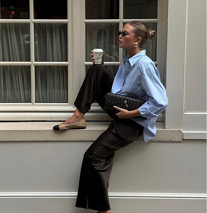 Camisa azul, pantalón negro de satén, bailarinas negras y beige y bolso negro.