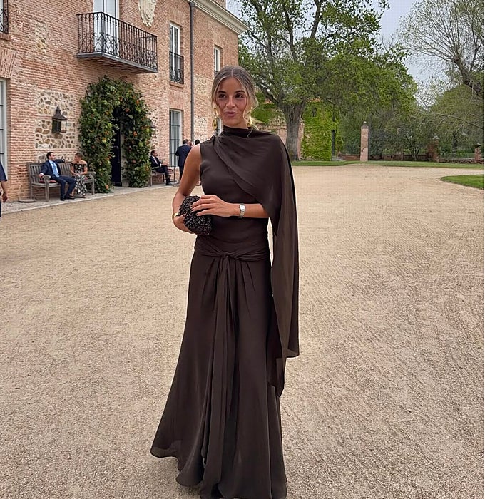 Vestido en marrón chocolate con un solo hombro y capa de gasa a juego con un bolso tipo 'clutch' negro.