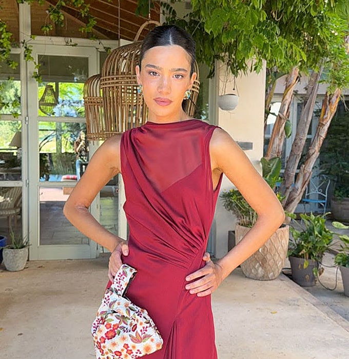 Vestido en rojo granate con drapeado y cuello alto combinado con un 'clutch' floral.