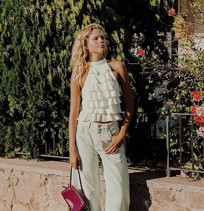 'Top halter' de volantes en capas en tono marfil sobre vaqueros anchos, con bolso de charol en fucsia.