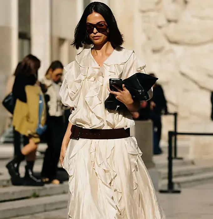 Vestido midi de volantes en crudo, cinturón de cuero oscuro y clutch negro.