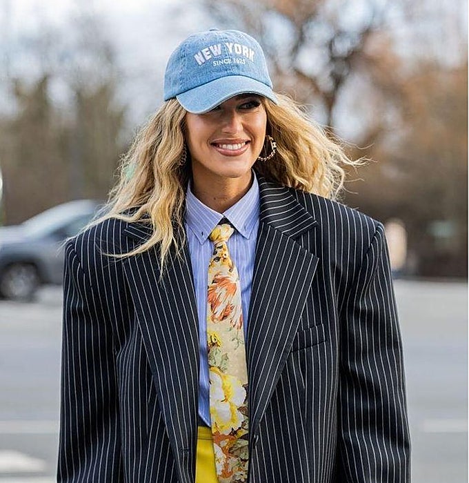 Americana 'oversized' de raya diplomática sobre camisa de rayas, con corbata floral y gorra vaquera.