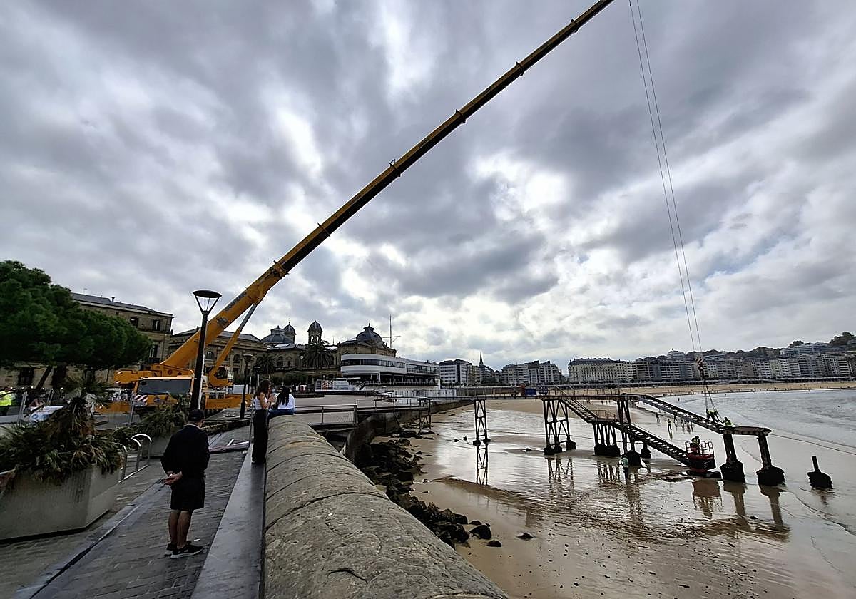 Una grúa de grandes dimensiones retira la escalera del embarcadero del Muelle