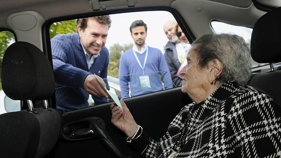 Una anciana de 98 años, ante la imposibilidad de acceder al colegio electoral, ejerce su derecho al voto entregando su papeleta al presidente de la mesa desde el coche. Efe