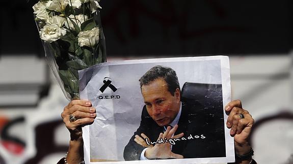 Una mujer enseña un cartel con la foto de Nisman y un ramo de flores durante una protesta.