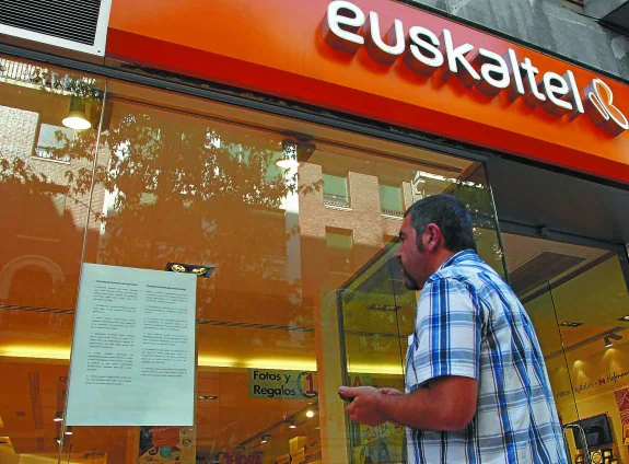 Un cliente observa un cartel con la reivindicación de los distrubuidores en una tienda de Euskaltel.