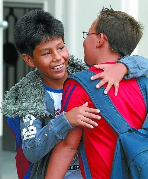 Dos alumnos de Primaria se abrazan a la entrada de un colegio. 