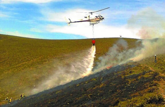 Bomberos intentando apagar un incendio con apoyo del helicóptero. 