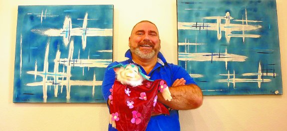 El autor y sus obras. Daniel Schvab Aguirregomezcorta entre dos de sus cuadros con el gnomo que protagoniza el vídeo-invitación a su exposición.