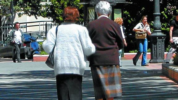 Dos mujeres mayores pasean del brazo por una plaza.