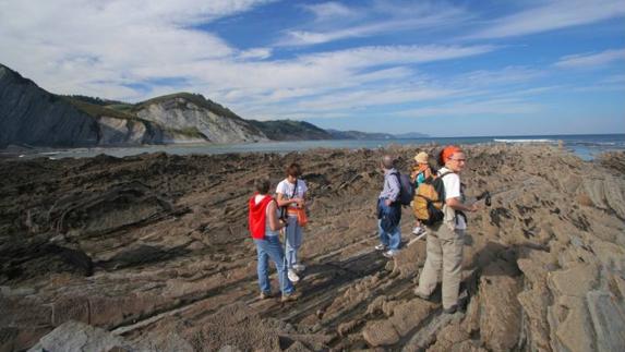 Foto; Un grupo de excursionistas pasea por la costa del Geoparque. Vídeo: Vídeo: El flysch, desde el mar. B.Campuzano / A.Múgica
