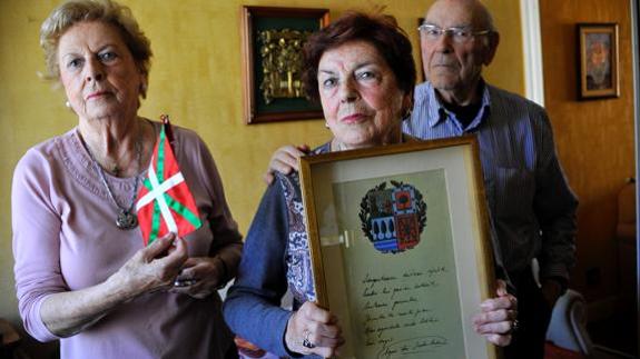 Los tres hermanos Aguirre-Amalloa posan en su casa con una reproducción del juramento del lehendakari. 