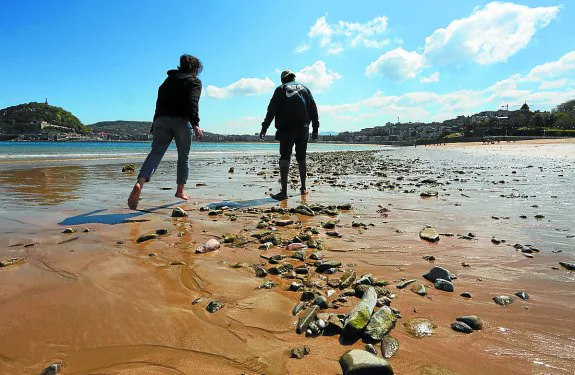Una pareja pasea por la orilla de Ondarreta, entre una gran cantidad de piedras. 