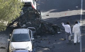 Dos especialistas se acercan al coche patrulla en el que viajaban los dos guardias civiles muertos por la explosión de la bomba. /AFP