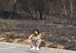 Una mujer habla por teléfono con el paisaje arrasado por el fuego en el pueblo de Médulas de fondo