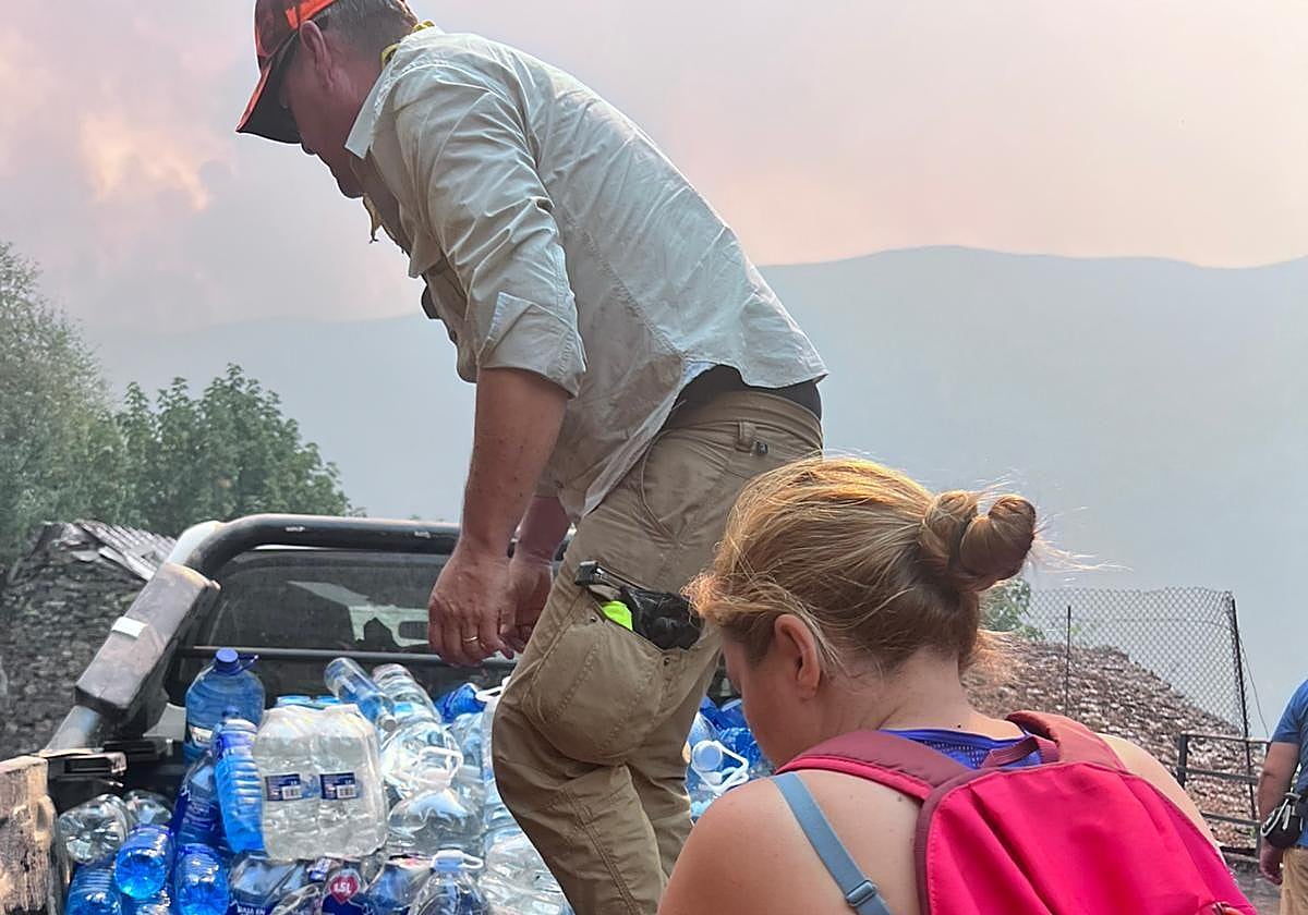 Vecinos de Peranzanes recogen las botellas de agua de avituallamiento de un vehículo con el incendio de fondo.