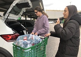 Dos estudiantes llenan el maletero de su coche con un carro cargado de garrafas en un supermercado de Ponferrada.