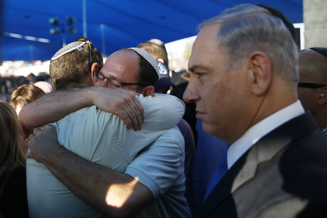 Benjamin Netanyahu con rostro serio junto a los padres de dos de los jóvenes asesinados, que lloran abrazados. 