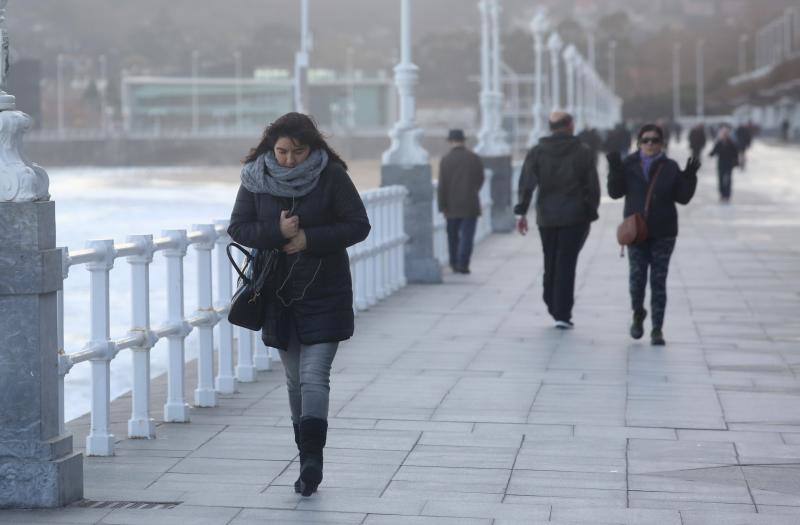Una mujer camina abrigada por el paseo del Muro de Gijón