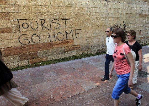 Varios viandantes pasan junto a la pared en la que se hizo la pintada contra los turistas. 