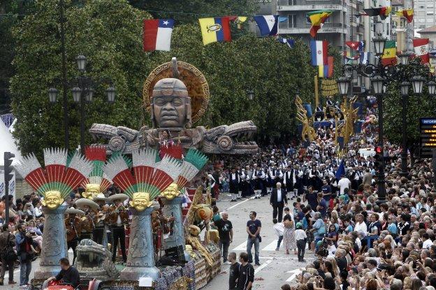 Una de las carrozas participantes en una edición anterior del desfile del Día de América en Asturias, seguida de la Real Banda de Gaitas Ciudad de Oviedo al principio de la calle Uría. 