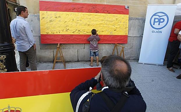 Imagen. Un niño firma la bandera de España colocada en el Parchís por Nuevas Generaciones de Gijón.