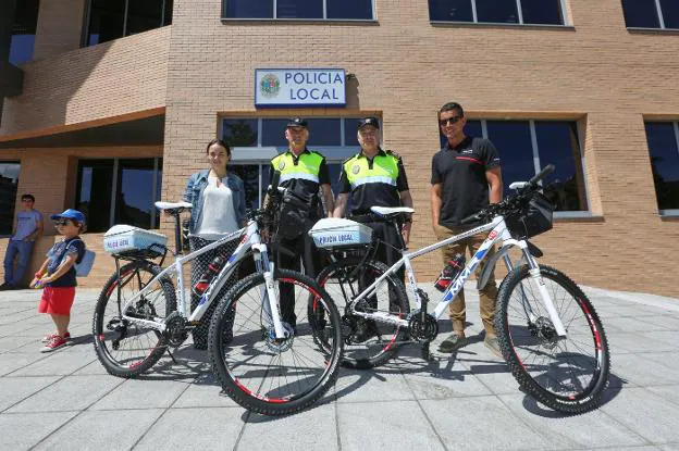 Agentes de la Policía Local junto a la concejala del área, Mar Iglesias, posan ante la comisaría junto a dos bicicletas en servicio durante la temporada estival 