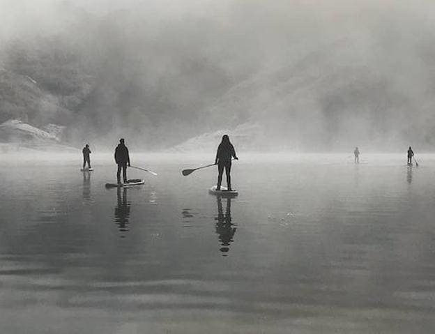 Un grupo de aficionados, disfrutando del padle surf durante bajo la niebla. 