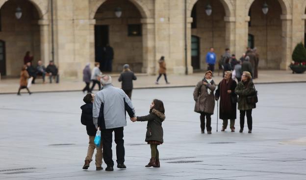 Una persona mayor pasea con dos niños por la plaza de España. 