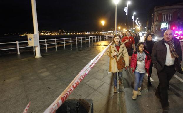 Imagen. Varios paseantes circulan en Gijón junto a una cinta que corta el paso en el Muro.