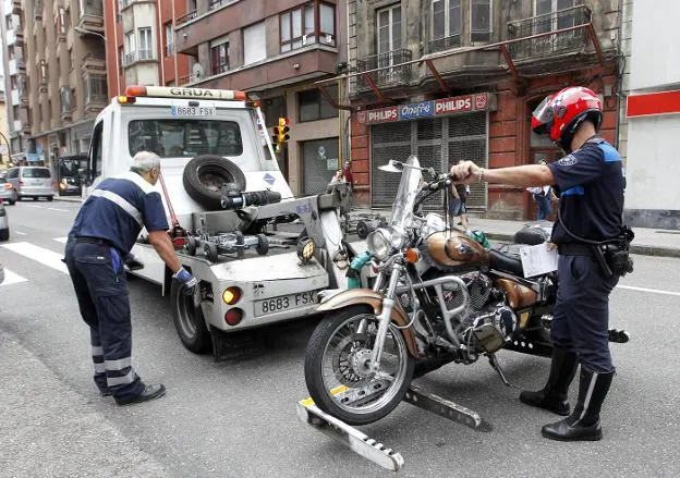 La grúa municipal se lleva una moto accidentada en la avenida de Hermanos Felgueroso con ayuda de un agente policial. 