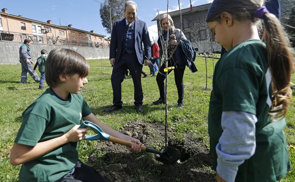 Wenceslao López y Alicia Castro atentos a dos niños mientras plantan un manzano. 