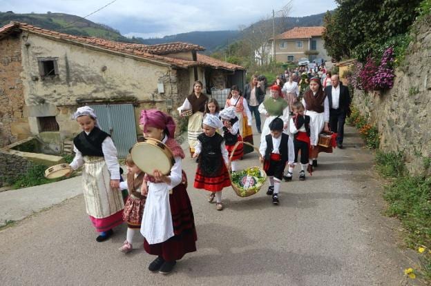 Niños y adultos, vestidos de asturianos, llevan el ramu y las ofrendas al santo antes de la misa solemne en la iglesia. 