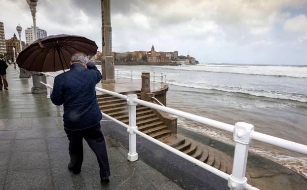 Un hombre se protege en Gijón de la lluvia y el viento en el mes de marzo. 