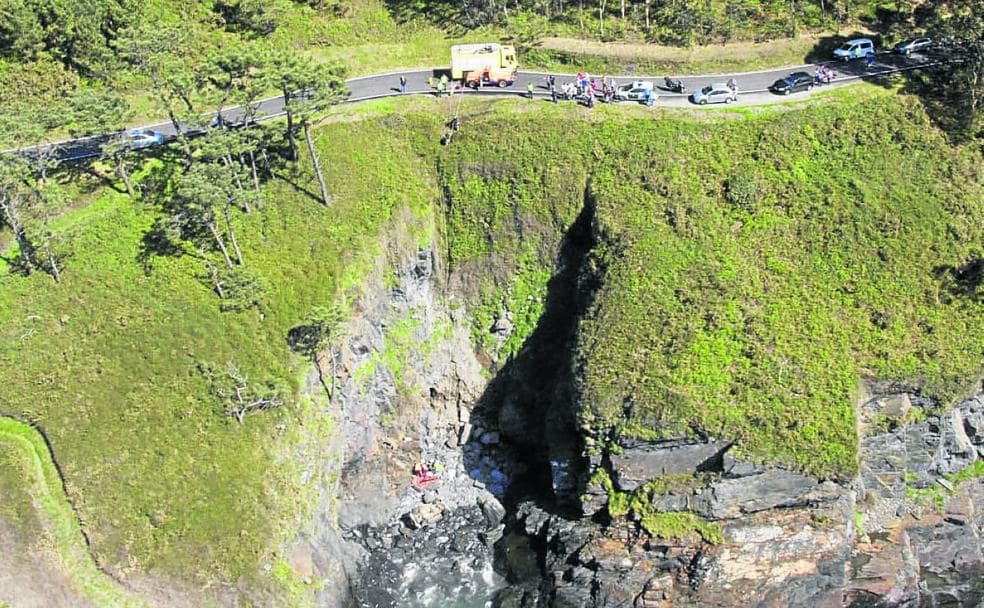 En el círculo, el vehículo cerca del agua, tras caer por el acantilado de una cala cercana al monolito de Navia. A la izquierda, los equipos de rescate auxilian al herido. 