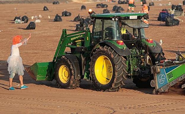 Un hombre disfrazado saluda a un operario de Emulsa durante la limpieza de la playa de Poniente tras la hoguera de San Juan. 