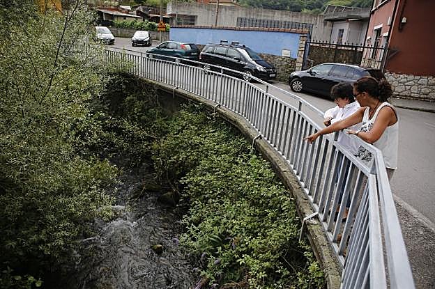 Silvia Suárez, con otra vecina, señala el río, con «malos olores debido a los vertidos» . 