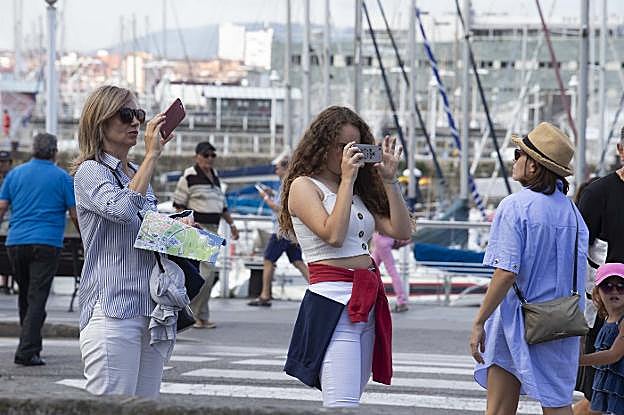Dos turistas, una de ellas con un plano de Gijón en la mano, hacen fotos desde el Muelle de Pelayo y la plaza del Marqués. 