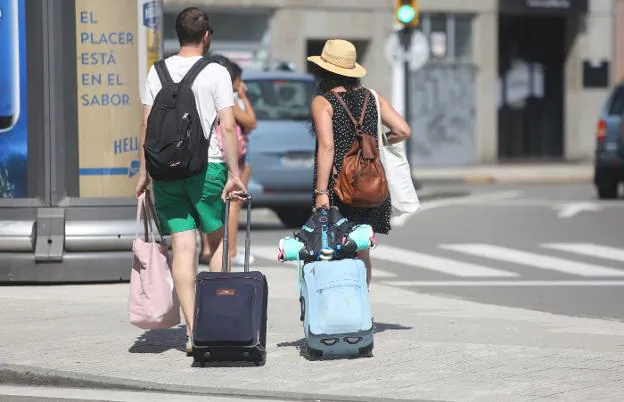Dos turistas pasean con sus maletas por Gijón. 
